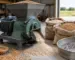 Moară de cereale cu ciocănele lângă saci cu cereale uscate într-un spațiu de lucru agricol