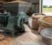 Moară de cereale cu ciocănele lângă saci cu cereale uscate într-un spațiu de lucru agricol