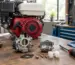 Carburator defect Honda GX analizat pe bancul de lucru, lângă un motor demontat