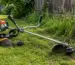 Motocoasa cu accesorii incluse folosită într-o gospodărie, lângă gard și vegetație de margine