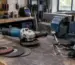 Polizor unghiular 125 mm pe banc de lucru într-un atelier, alături de discuri și echipament de protecție